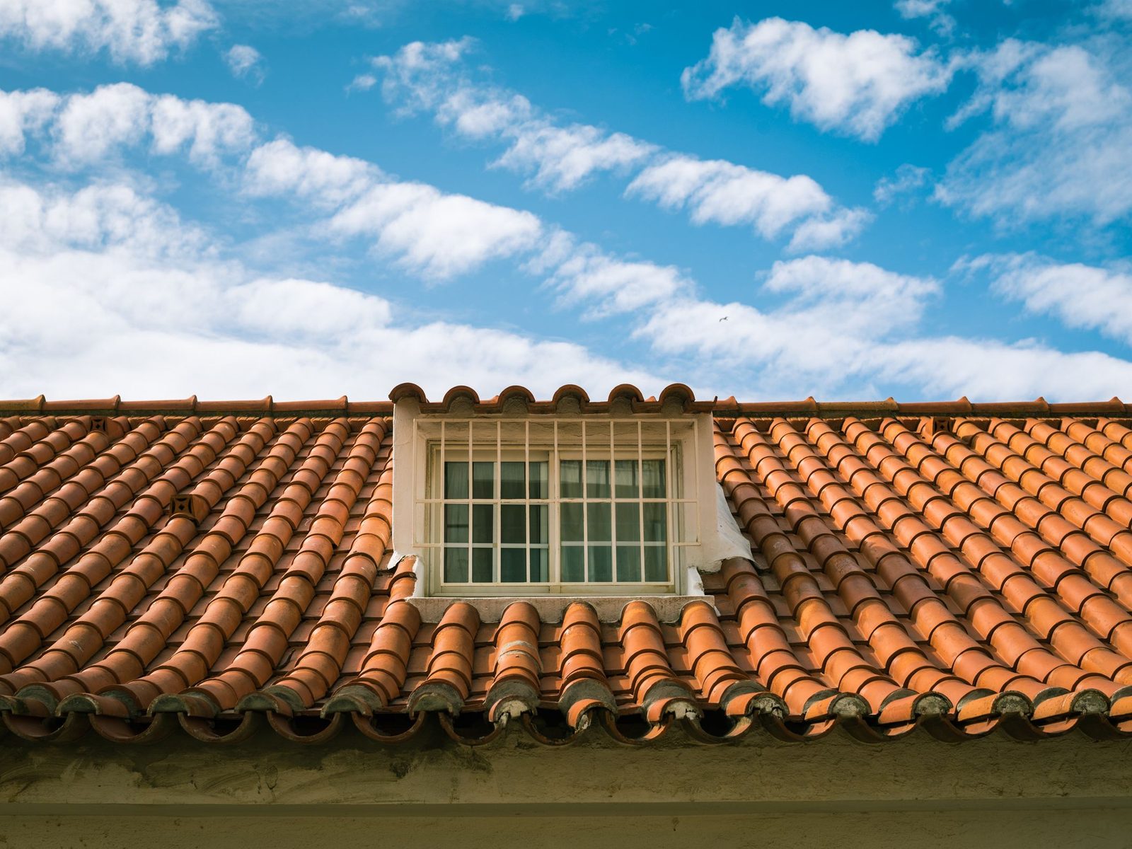 Clay tile roof with a dormer window under a blue sky